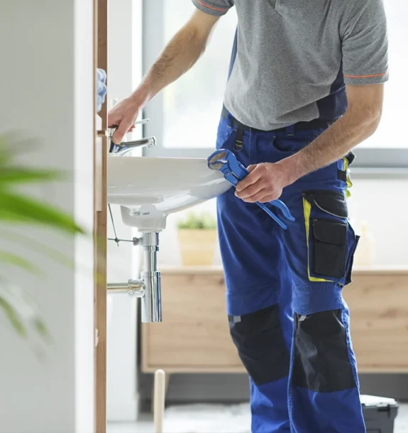 En VVS-montör i arbetskläder servar ett tvättställ med en blå rörtång. Rörmokare på Gotland.