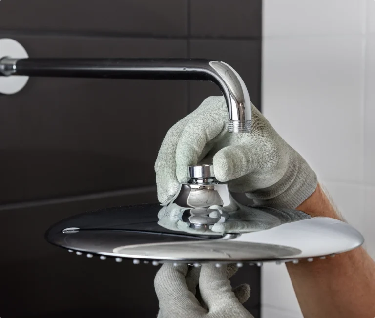 Närbild på händer i grå skyddshandskar som monterar ett stort, runt duschhuvud i krom.