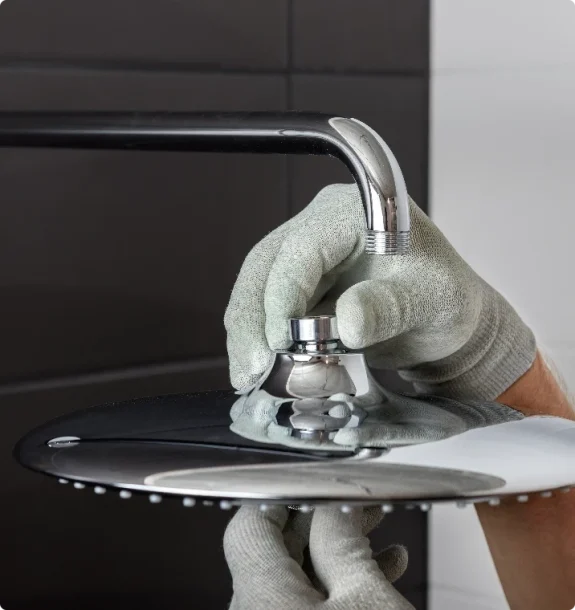 Närbild på händer i grå skyddshandskar som monterar ett stort, runt duschhuvud i krom.