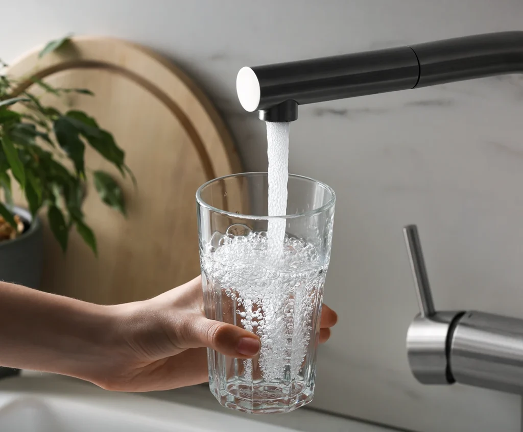 Hand fyller ett glas med vatten vid en svart köksblandare